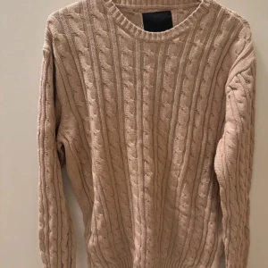 Beige stickad tröja - Säljer en mysig beige stickad tröja med kabelstickat mönster. Tröjan har långa ärmar och en rund halsringning, perfekt för kyliga dagar.