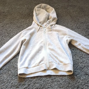 Grå hoodie från Gina Tricot - Säljer en stilren grå hoodie från Gina Tricot med dragkedja framtill. Perfekt för en avslappnad look. Den har en klassisk huva och långa ärmar.