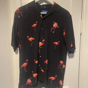 Kortärmad skjorta - Snygg svart kortärmad skjorta från Jack & Jones med ett flamingomönster. Mycket bra skick. 