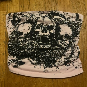 Rosa tubhalsduk med dödskallemönster - Cool rosa tubhalsduk med ett svart dödskallemönster. Perfekt för att ge en edgy touch till din outfit. Materialet är mjukt och bekvämt, idealiskt för kyligare dagar.