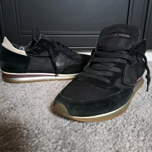 Svarta Phillipe Model skor - Snygga svarta sneakers med mockadetaljer och vita inslag. Skorna har en klassisk design med snörning och en bekväm sula. Perfekta för en stilren look. Kom gärna med pris förslag.