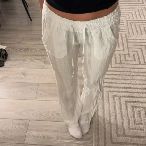 Vita lågmidjade linnebyxor - Snygga vita lågmidjade linnebyxor från Chelsea med elastisk midja för extra komfort. De är bootcut/raka i modellen. Tillverkade i Italien. De är helt nya och oanvända alltså i nyskick. 