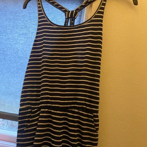 Randig byxdress i marinblå och vit - Säljer en superfin randig byxdressi marinblå och vit. Den har en bekväm passform och är perfekt för sommardagar. Byxdressen har ett knytband i ryggen och är ärmlös, vilket gör den luftig och skön att bära. Perfekt för både vardag och festliga tillfäl