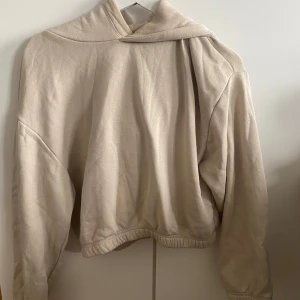 Beige hoodie - Säljer en mysig beige hoodie i normal passform. Den är perfekt för höst och vinter med sin mjuka och varma känsla. Hoodien har långa ärmar och en klassisk huva samt ett elastiskt band nertill som får den att följa kroppen på ett fint sätt!