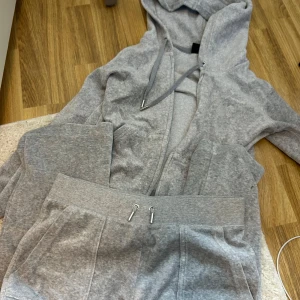 Grå hoodie från Juicy Couture - Säljer en supermjuk och bekväm grå hoodie från Juicy Couture. Den har en dragkedja framtill och en praktisk ficka med knappar. Perfekt för en avslappnad dag eller mysiga stunder hemma. Passar perfekt till höst och vinter!
