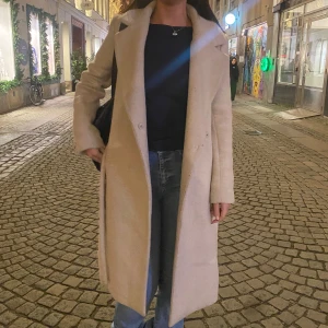 Beige kappa med bälte - Säljer en superfin beige kappa med bälte i midjan. Perfekt för höst och vinter! Den har en figursydd design med långa ärmar och en stilren look. Passar både till vardags och fest. 🧥✨