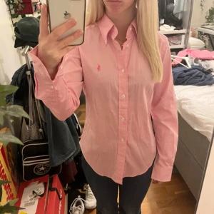 Rosa skjorta från Ralph Lauren - Säljer en snygg rosa skjorta från Ralph Lauren i storlek dam S. Skjortan är i nytt skick med etikett kvar. Den har långa ärmar och klassiska knappar framtill. Perfekt för både vardag och fest! 💖