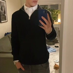 Svart halfzip - Säljer en stilren svart tröja med dragkedja i kragen. Perfekt för både vardag och lite finare tillfällen. Tröjan har en normal passform och är långärmad, vilket gör den idealisk för höst och vinter. Den är i mycket bra skick och passar perfekt över en skjorta. Sitter som m. Jag är 182 