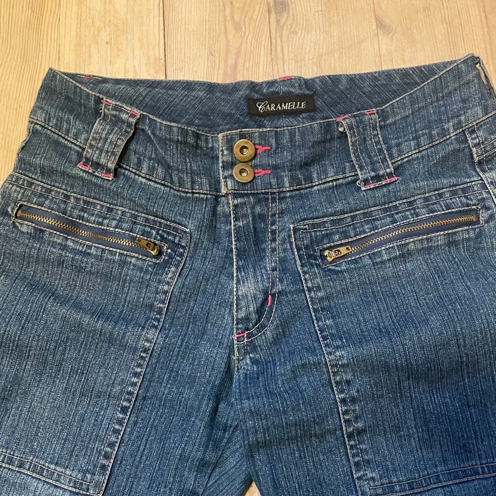 Säljer ett par snygga blå jeans från Caramelle med coolt rosa fjärilsbroderi på bakfickorna. De har en straight/bootcut ish passform och är lågmidjade med dubbla knappar och dragkedjor fram. Dom är nerklippta där nere för att dom ska passa mig som är 160cm lång, men dom är fortfarande lite långa på mig💝.. Jeans & Byxor.