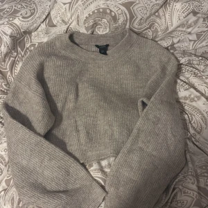 Grå croppad stickad tröja från Garage - Säljer en superfin grå croppad stickad tröja från Garage. Perfekt för höst och vår med sin mysiga och stilrena design. Tröjan har långa ärmar och en ribbad struktur som ger en skön passform. Passar perfekt till både jeans och kjol!