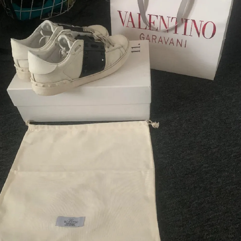 Säljer ett par snygga Valentino sneakers i vitt med en cool svart detalj över snörningen. De är i bra skick och kommer med originalförpackning och dustbag. Perfekta för att ge din outfit en lyxig touch!. Skor.