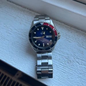 Orient dykkarklocka med stållänk - Säljer en snygg Orient klocka i mycket bra skick. Den har en blå urtavla med datumvisning. Armbandet är i rostfritt stål. Urtavlan är automatiskt vilket innebär att den inte har något batteri utan drivs av energin på handleden. Klockan är vattentät och verktyg och extra delar till armbandet kommer med för att ändra storlek 