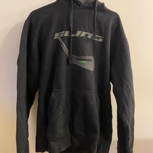Svart hoodie med tryck - Säljer en svart hoodie med coolt tryck på framsidan. Den har en klassisk passform med långa ärmar och en praktisk ficka framtill. Perfekt för en avslappnad stil eller att mysa i hemma. Passar till både höst och vinter.