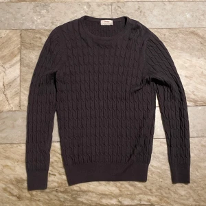 Mörkgrå stickad tröja från Gran Sasso - Säljer en snygg mörkgrå stickad tröja från Gran Sasso, tillverkad i Italien. Tröjan har ett klassiskt kabelstickat mönster och långa ärmar. Perfekt för kyliga dagar och ger en stilren look. Passar både till vardags och lite finare tillfällen.