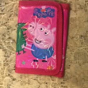 Peppa Pig Barn plånbok - Söt rosa plånbok med Peppa Pig-motiv. Perfekt för barn som älskar Peppa Pig! Plånboken har en praktisk design med plats för mynt och sedlar. Den är gjord i syntetmaterial och har en färgglad och lekfull stil.   Finns fler kvar, sammafrakt 