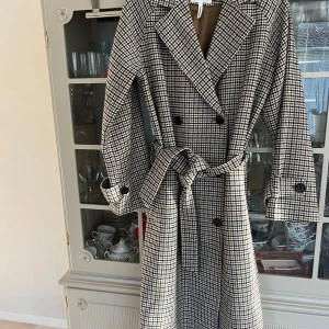 Rutig kappa från OBJECT - Säljer en superfin rutig kappa från OBJECT i storlek 36. Den har ett klassiskt mönster i svart, beige och brunt med knappar och ett bälte i midjan. Perfekt för höst och vår! Kappan är i mycket bra skick och har långa ärmar. Passar både till vardags och lite finare tillfällen.