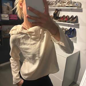 Säljer en elegant beige blus med en stor rosett vid halsen. 