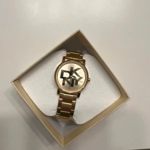Guldfärgad klocka från DKNY - Snygg guldfärgad klocka från DKNY med ett stilrent armband i metall. Urtavlan har en cool design med stora bokstäver. Perfekt för både vardag och fest! Kommer i originalförpackning.