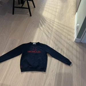 Mörkblå tröja från Moncler - Säljer en snygg mörkblå tröja från Moncler i storlek S. Tröjan har ett coolt rött broderat Moncler-logotyp på framsidan. Perfekt för höst och vinter, med långa ärmar och en bekväm passform. Passar både till vardags och lite finare tillfällen. 🧥✨