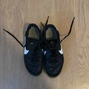 Nike Premier i svart och vitt - Säljer ett par Nike Premier futsal skor i svart och vitt. Skorna har en klassisk design med snörning och en bekväm gummisula. Perfekta för träning. De är i bra skick med lite slitage på sulan. Passar perfekt för dig som gillar stilrena och sportiga skor.
