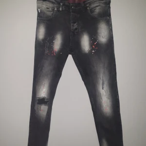 Svarta jeans med slitningar från Jack & Jones - Säljer ett par svarta jeans från Jack & Jones i slim fit. De har coola slitningar och en unik tvättad look med röda detaljer. Perfekta för en avslappnad stil eller en utekväll. De är i bra skick och redo för nya äventyr!