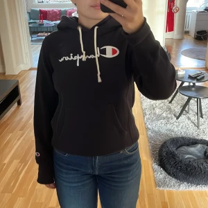 Svart hoodie från Champion - Säljer en svart hoodie från Champion i storlek medium. Den har en klassisk design med Champion-loggan broderad på bröstet och en liten logga på ärmen. Hoodien är i bra skick då den endast är använd enstaka gånger och perfekt för höst och vinter. Den har en skön passform och är gjord i ett mjukt material ✨