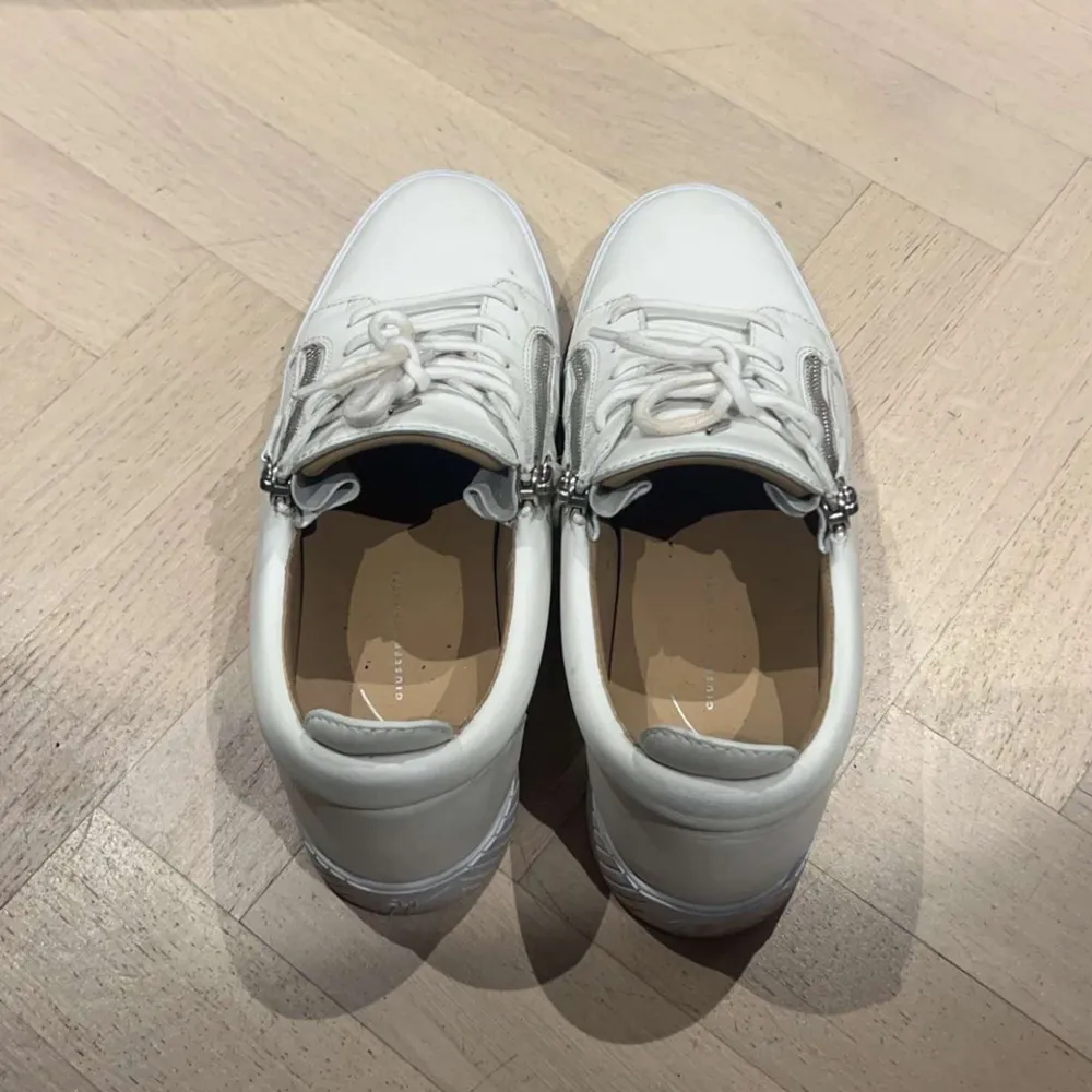 Säljer ett par stilrena vita sneakers i skinn med både snörning och dragkedja på sidan. Perfekta för en casual look och passar till nästan allt. De är i mycket bra skick och har en snygg, minimalistisk design.. Skor.