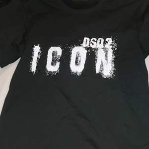 Säljer en svart t-shirt från DSQ2 i storlek S. Den har en cool vit text 'ICON' på framsidan som ger en trendig look. Perfekt för vardagsbruk eller en avslappnad utekväll. Tillverkad i Italien, vilket garanterar hög kvalitet. Passar perfekt till jeans eller shorts!