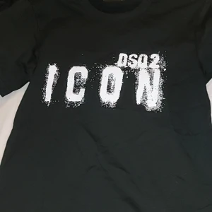 Svart t-shirt från DSQ2 - Säljer en svart t-shirt från DSQ2 i storlek S. Den har en cool vit text 'ICON' på framsidan som ger en trendig look. Perfekt för vardagsbruk eller en avslappnad utekväll. Tillverkad i Italien, vilket garanterar hög kvalitet. Passar perfekt till jeans eller shorts!