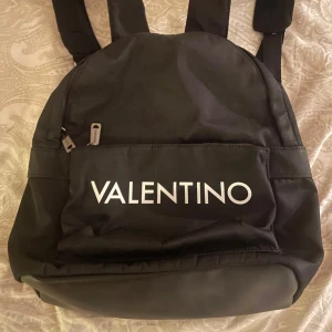 Svart ryggsäck från Valentino - Snygg svart ryggsäck från Valentino i mycket bra skick. Den har en praktisk dragkedja framtill och justerbara axelremmar. Perfekt för både vardag och resa. Stilren design med tydlig logga på framsidan. Ny pris 1500kr