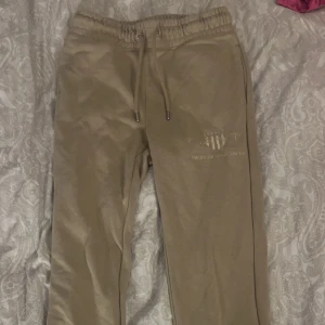Beige mjukisbyxor från GANT - Säljer ett par superbekväma beige mjukisbyxor från GANT i storlek XS. De har en elastisk midja med snörning och GANT-loggan broderad på sidan. Perfekta för en avslappnad dag hemma eller en snabb tur till affären. 🛍️