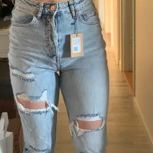 Säljer ett par snygga ljusa jeans med hög midja och hål på knäna. De har en bootcut-stil och är tillverkade i jeansmaterial. Perfekta för en avslappnad och trendig look! Mycket bra skick!