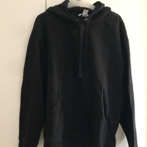 Svart hoodie - Säljer en klassisk svart hoodie i bra skick. Den har en bekväm passform med långa ärmar och en praktisk huva med dragsko samt fickor framtill. Perfekt för kyliga dagar eller som ett stilrent basplagg i garderoben.
