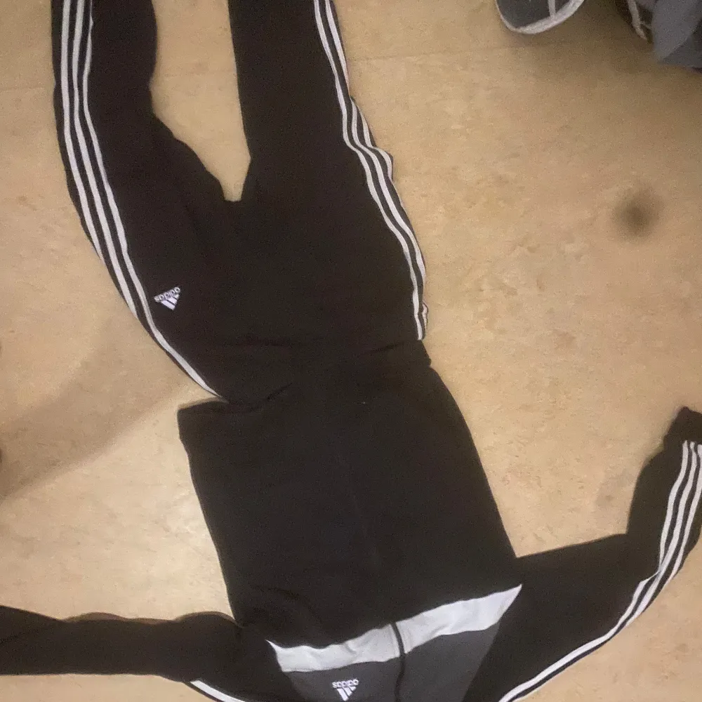 Säljer två tracksuits från Adidas i svart och mörkblått. De har de klassiska tre vita ränderna längs sidorna och en liten Adidas-logga på låret. Perfekta för träning eller chill hemma. Superbekväma och i bra skick!  Båda för 500kr eller 300kr/st priset kan diskuteras.. Hoodies.