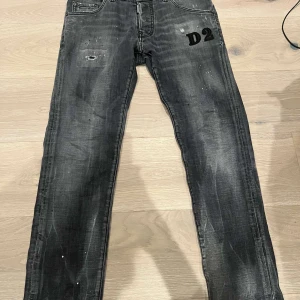 Svarta jeans från Dsquared2 - Säljer ett par coola svarta jeans från Dsquared2 i storlek 16Y. De har en sliten look med små hål och färgstänk för en edgy stil. Perfekta för både vardag och fest! 🖤nypris ligger på 4,700. I bra skick! 