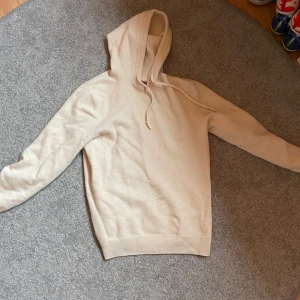 Beige hoodie i merinoull - Säljer en snygg beige hoodie i bomull. Den är supermjuk och perfekt för både höst och vår. Tröjan har en normal passform med långa ärmar och en klassisk huva med dragsko. Perfekt för en avslappnad stil!