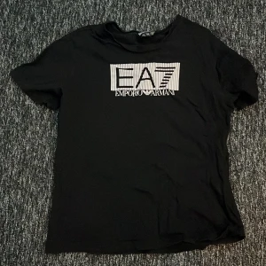 Svart t-shirt från Emporio Armani - Säljer en svart t-shirt från Emporio Armani med EA7-logga på bröstet. Den är i bra skick och perfekt för vardagsbruk. T-shirten har en normal passform och är kortärmad, vilket gör den idealisk för både vår och sommar.