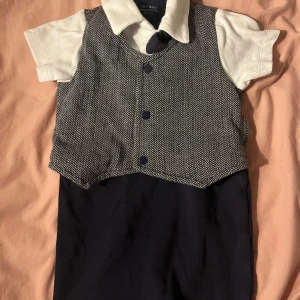Baby kostym - Säljer en supergullig baby kostym från Next i riktigt bra skick. Västen har ett klassiskt fiskbensmönster i grått och vitt med mörkblå knappar. Perfekt för små festliga tillfällen! 💙