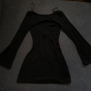 Svart klänning med knytband - Snygg svart klänning med långa ärmar och knytband i ryggen. Perfekt för en kväll ute eller en fest. Den har en tight passform som framhäver figuren och är gjord i ett mjukt material för extra komfort.🖤⏳