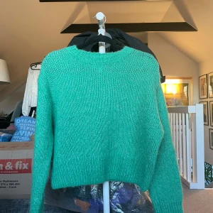Grön stickad tröja - Säljer en härlig grön stickad tröja med långärmad design. Perfekt för kyligare dagar med sin mysiga och varma känsla. Tröjan har en enkel och stilren look som passar till många olika outfits. Är i storlek xs, men passar s.