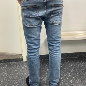Blå jeans med broderad detalj - Snygga blå jeans från nudie jeans med en broderad nudie märke på bakfickorna. De har en slim passform och är midwaist. Perfekta för en stilren look.