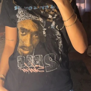 Svart t-shirt med tryck - Cool svart t-shirt med ett stort tryck av en känd artist på framsidan. T-shirten har korta ärmar och en normal passform, perfekt för en avslappnad stil. Ett måste för musikälskare!