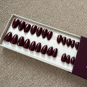 Vinröda lösnaglar från Switch Nails - Snygga vinröda lösnaglar från Switch Nails i modellen 'Cherry Noir'. De är återanvändbara och tillverkade av återvunnet material. Perfekt för en snabb och stilren manikyr hemma. 2 naglar saknas.