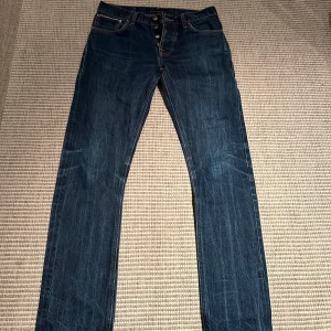 Nudie jeans grim Tim dry selvage - Tjena säljer nu dessa riktigt snygga och fräscha nudie selvage jeans i en fin mellanblå färg. Storleken är 32/34 men sitter mer som 30/32 på grund ut av tvättningar som dem krympt lite. Modellen heter Grim Tim och är den populäraste modellen. Jeansen är i väldigt bra skick runt omkring 9/10 och anledning till att jag säljer är just för att den blivit för små! Skriv privat vid frågor eller funderingar!