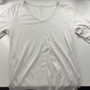 Vit ribbad långärmad topp - Säljer en stilren vit ribbad topp med v-ringning. Den har långa ärmar.Likadan som den svarta som ligger uppe. Från lager 157.storlek s men passar även xs.