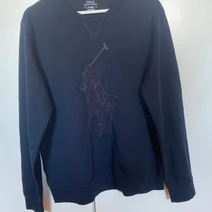 Mörkblå tröja från Polo Ralph Lauren - Säljer en stilren mörkblå sweatshirts från Polo Ralph Lauren med ett diskret broderat polospelarmotiv på framsidan. Tröjan har långa ärmar och en klassisk rund halsringning. Storlek M, aldrig använd!
