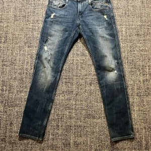 Blå Replay jeans med slitningar - Snygga blå jeans från Replay med coola slitningar för en trendig look. De har en dragkedja och knapp framtill samt klassiska fem fickor. Perfekta för en avslappnad stil.