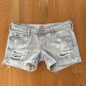 Grå jeansshorts från Hollister - Snygga grå jeansshorts från Hollister med slitna detaljer och fransar. Perfekta för en avslappnad stil. De har en låg midja och klassisk femficksdesign. Dem är helt perfekt low waist! Alltså väldigt low waist! Grenhöjd: 14 cm Midjemått: 37 cm rakt över💞💞