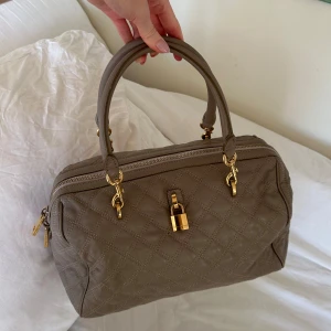 Beige quiltad handväska från Marc Jacobs! - Snygg beige handväska i quiltat skinn med guldfärgade detaljer. Väskan har dubbla handtag och en säker dragkedja upptill. Perfekt för att ge din outfit en lyxig touch. Dekorativt lås fram och en ficka baktill. Passar både till vardags till skola eller jobb men även en rymlig väska för annat. Mått 35x25x20 cm. Jättefint skick, inget att anmärka på!🤎