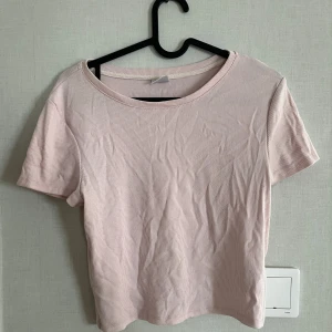 Ljusrosa ribbad topp från Gina Tricot - Säljer en söt ljusrosa ribbad topp från Gina Tricot. Toppen har korta ärmar och en rund halsringning, perfekt för sommaren. Den är i en mjuk och bekväm. Den är lite kroppad.